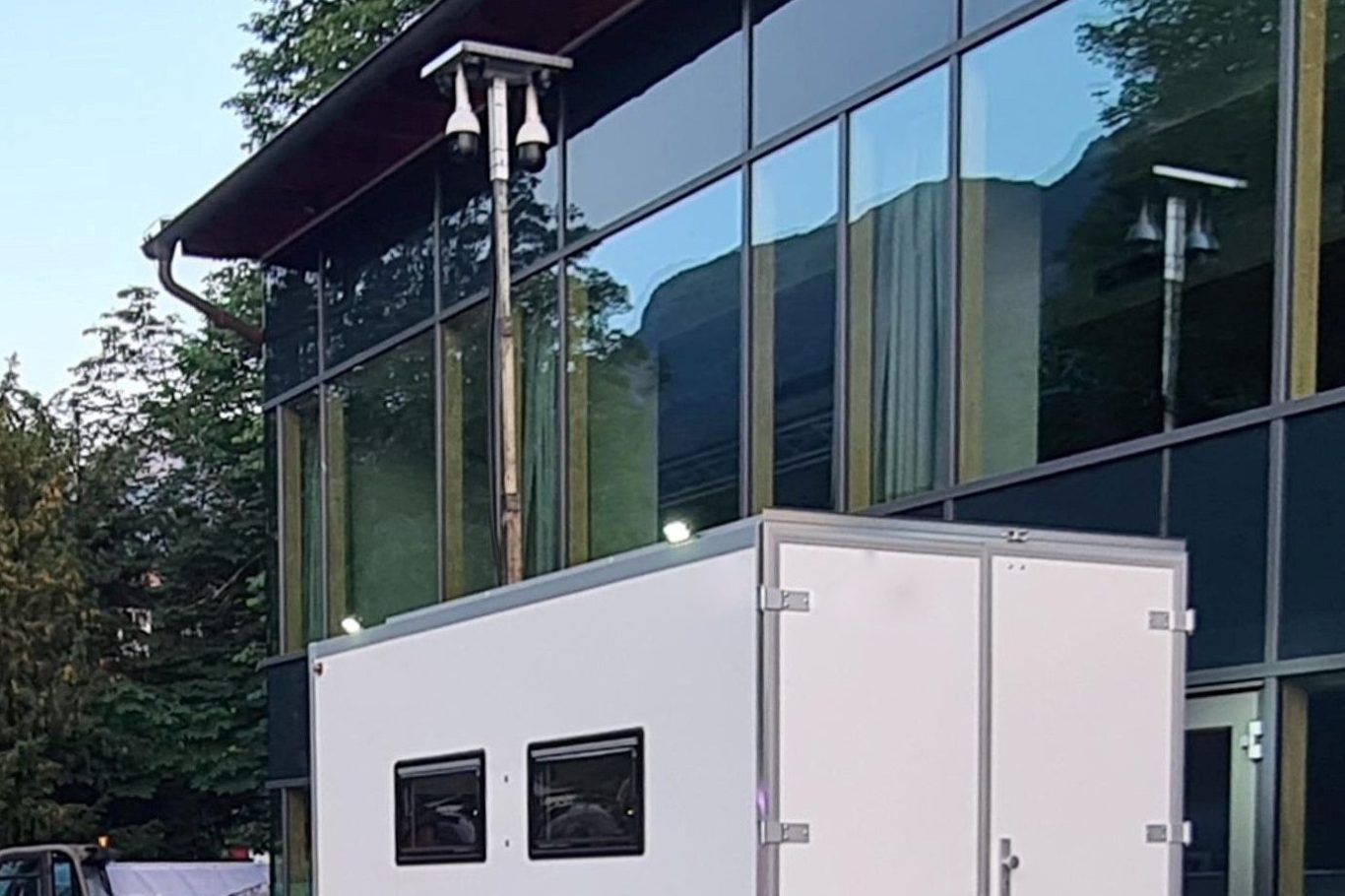 Weiße Container vor einem modernen Gebäude mit großen Glasfenstern.