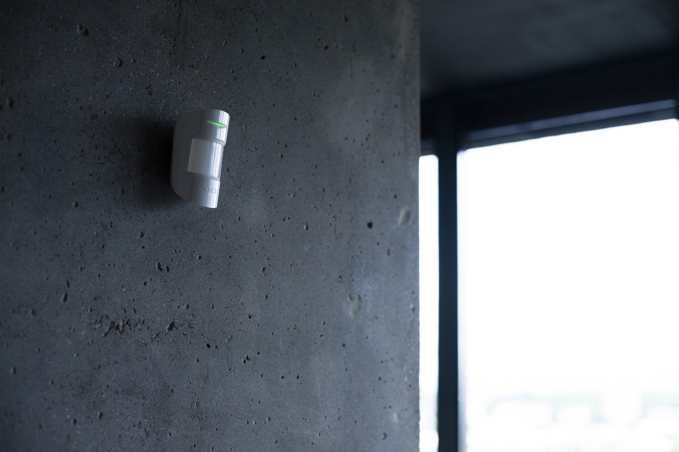 Bewegungsmelder Bewegungsmelder an einer betonfarbigen Wand neben einem Fenster.