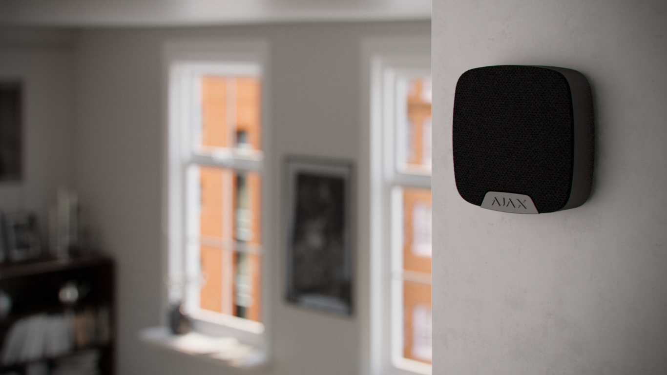 Innensirene Schwarzes Gerät an der Wand in einem hellen Raum mit Fenstern und Bücherregal.