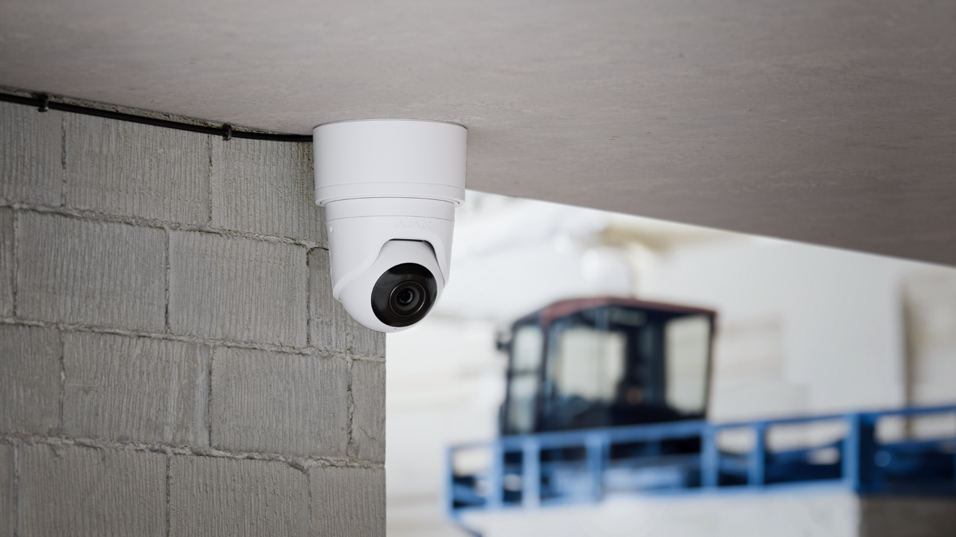 Überwachungskamera außen Sicherheitskamera an einer Wand in Innenraum, im Hintergrund ein Fahrzeug erkennbar.